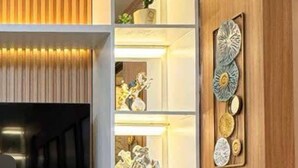 A modern living room with a flat-screen TV mounted on a white wall, wooden paneling, and built-in shelves displaying decorative items and plants. - MJM Cityscape At Red Residences Makati (Makati)