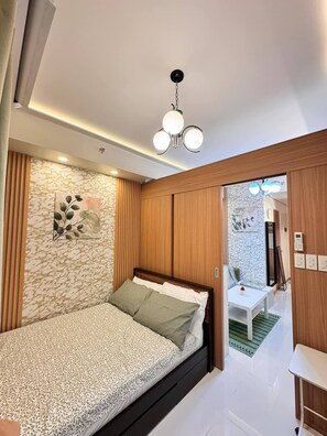 A modern bedroom with a bed, a small table, and a wall-mounted light fixture. - MJM Cityscape At Red Residences Makati (Makati)
