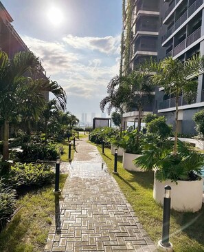 A pathway leading to a modern building with a glass facade, surrounded by lush greenery and palm trees. - MJM Cityscape At Red Residences Makati (Makati)