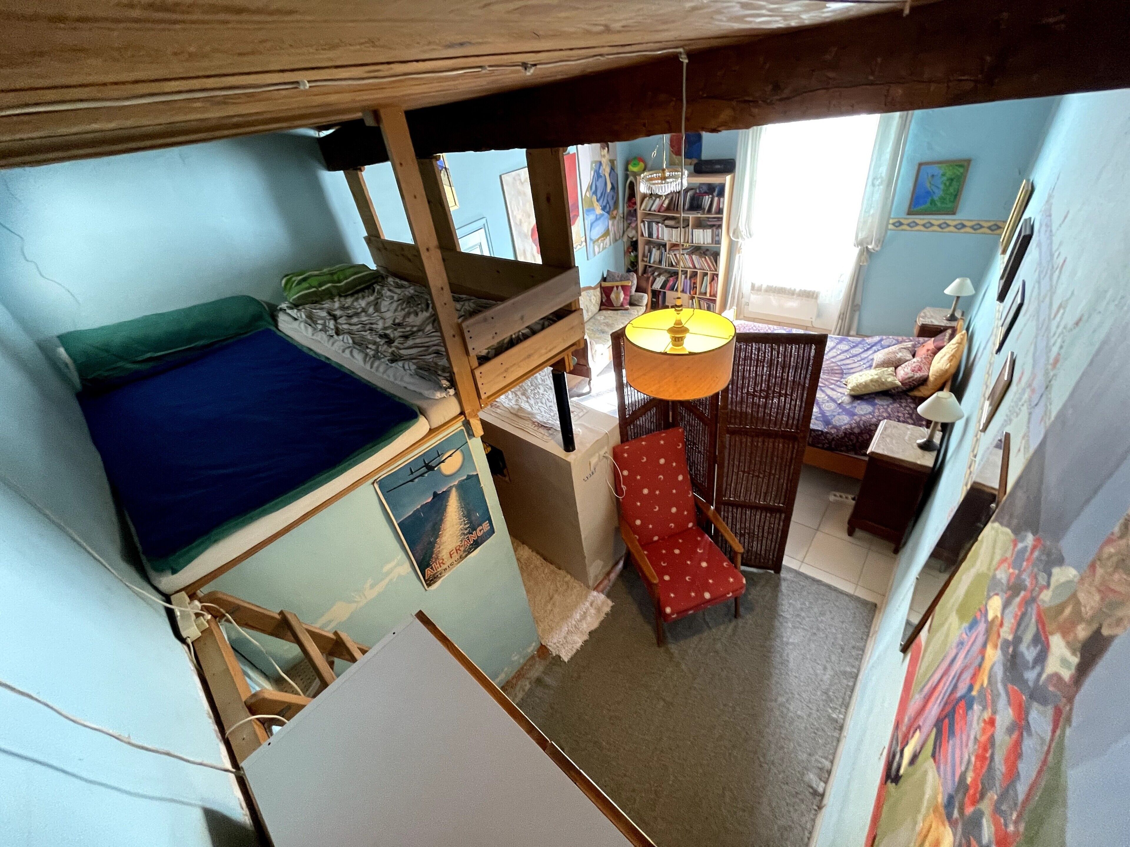 Een kamer met een stapelbed, een bureau, een stoel, een boekenplank en een hanglamp.
