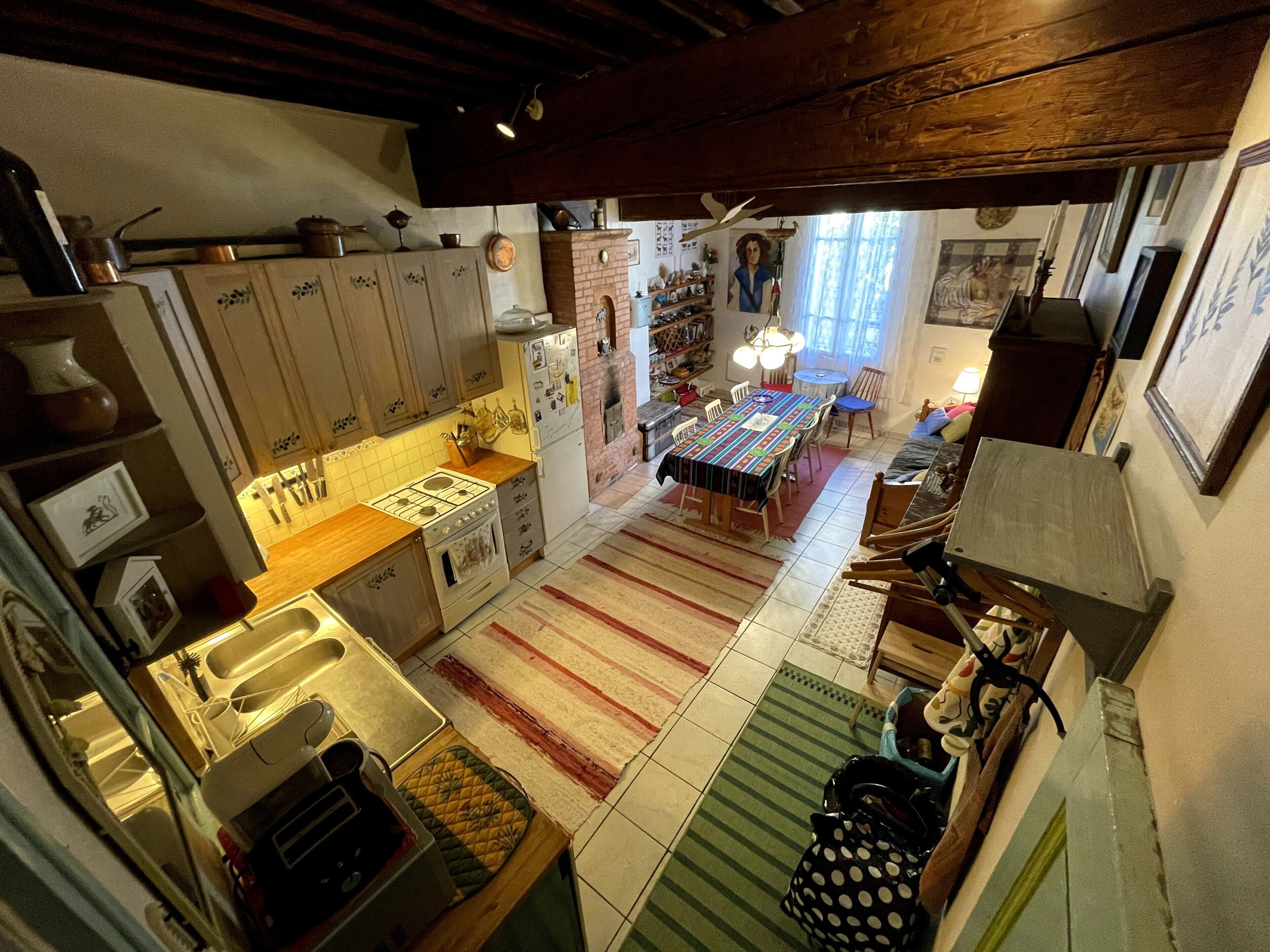 Een keuken met een fornuis, gootsteen en kasten, een eethoek met een tafel en stoelen, en een woonruimte met een bank en een televisie.