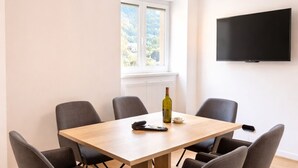 Ein moderner Konferenzraum mit einem Holztisch, sechs grauen Stühlen, einer Weinflasche und einer Fernbedienung.