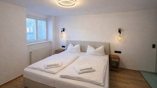 Ein modernes Schlafzimmer mit einem großen Bett, zwei Nachttischen, einem Fenster und Wandleuchten.