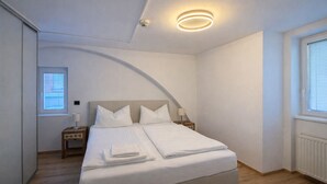 Ein Schlafzimmer mit Bett, Nachttischen, einem Fenster und einer Deckenleuchte.