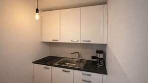 Eine kleine Küche mit weißen Schränken, einer schwarzen Arbeitsplatte, einem Edelstahl-Spülbecken und einer Kaffeemaschine.