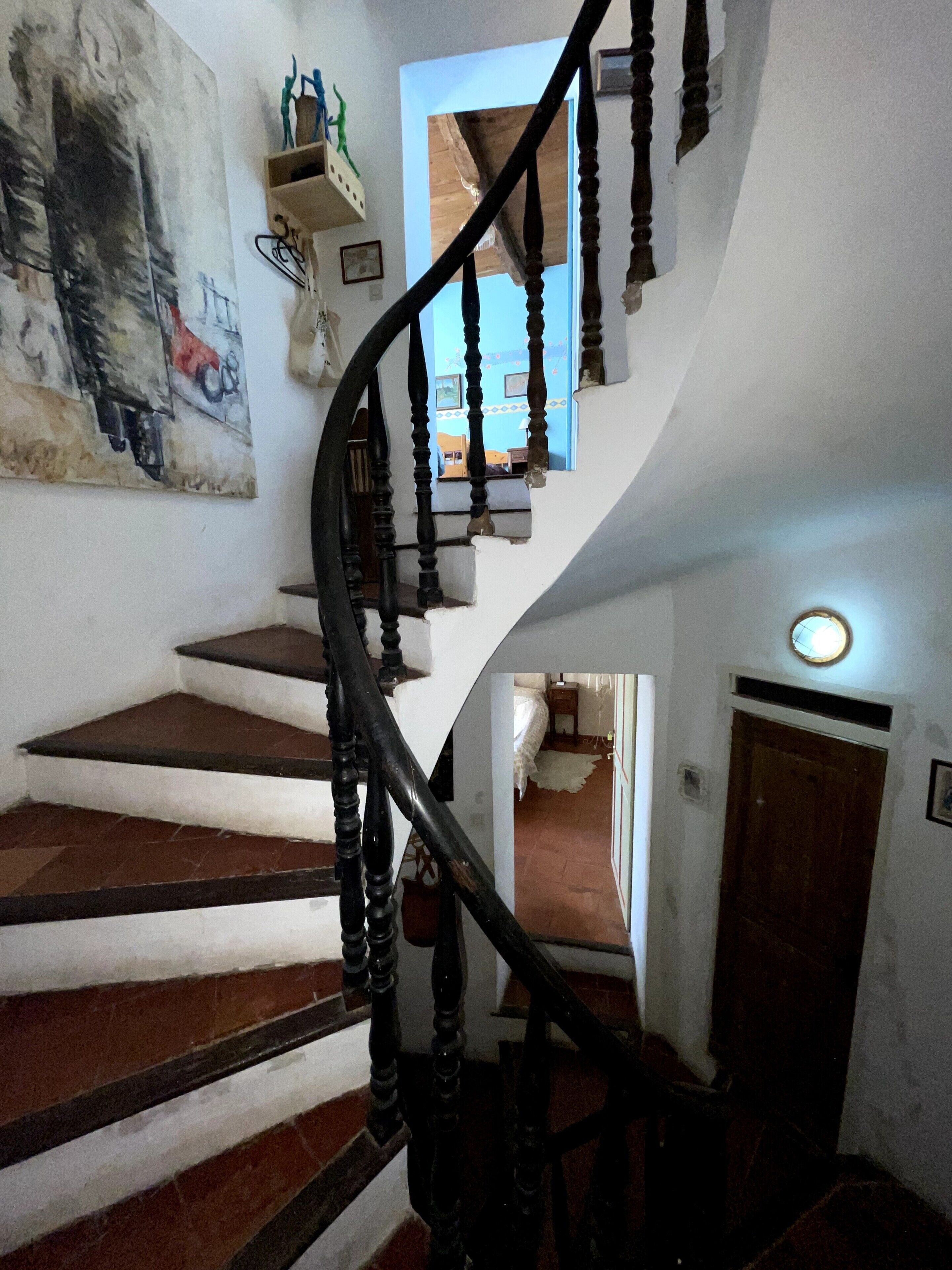 Eine Wendeltreppe mit Holzhandlauf, ein Gemälde an der Wand und eine Tür am Fußende.