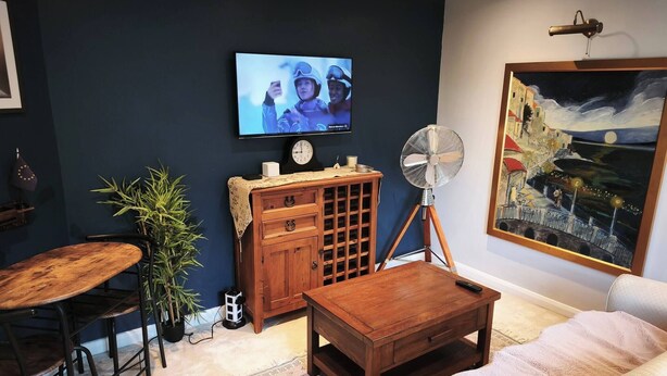 A living room with a TV, wooden furniture, a fan, and a painting on the wall. - Groombridge 1 Bed Self Catered Flat, can Sleep 4 (Royal Tunbridge Wells)
