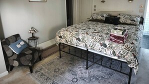 A bedroom with a large bed, a small side table, a chair, a rug, and a painting on the wall. - Groombridge 1 Bed Self Catered Flat, can Sleep 4 (Royal Tunbridge Wells)