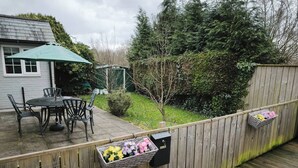 A wooden deck with a table and chairs, surrounded by a wooden fence, and a small garden area with flowers. - Groombridge 1 Bed Self Catered Flat, can Sleep 4 (Royal Tunbridge Wells)