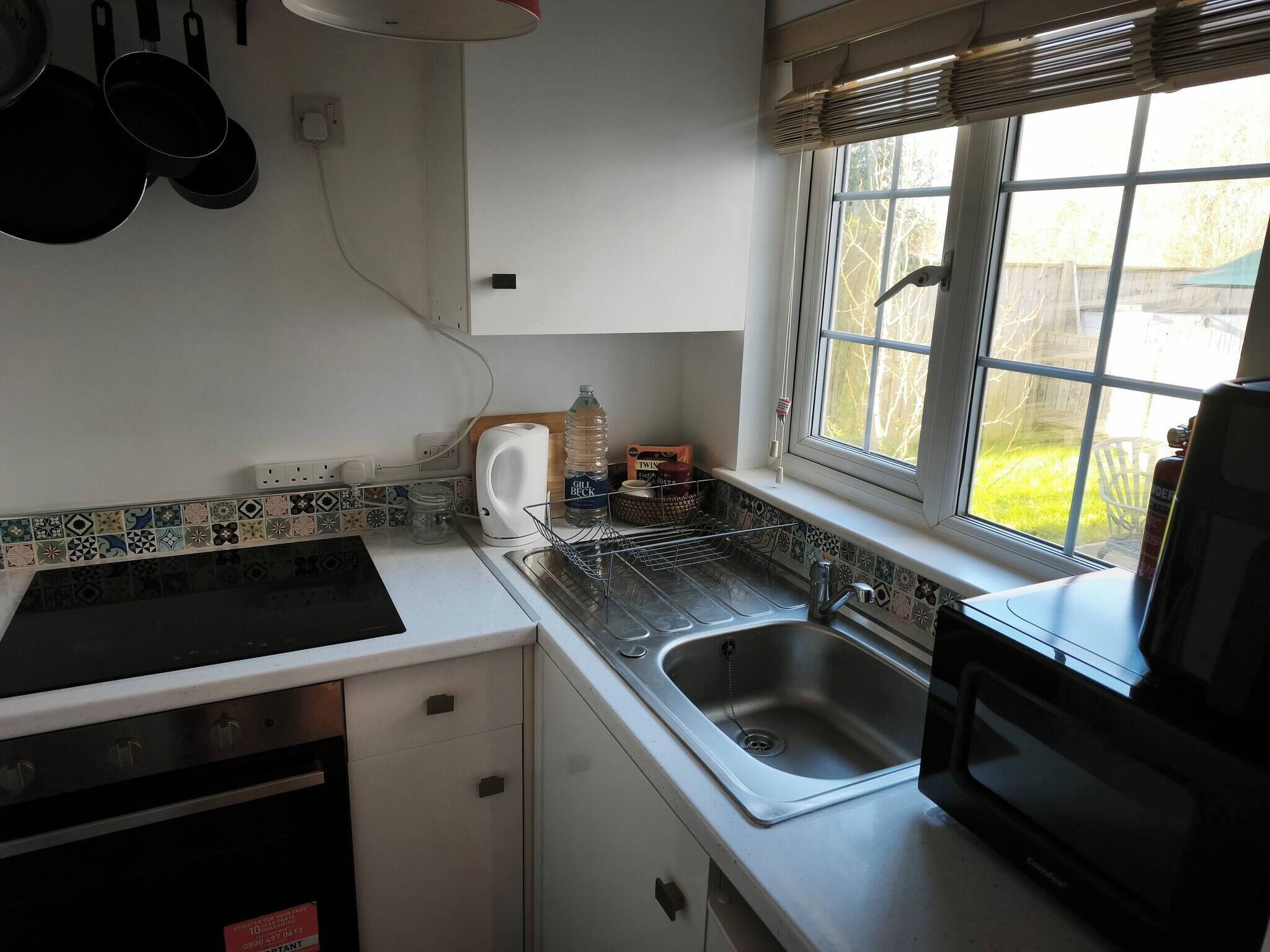 Una cucina con lavandino in acciaio inox, un forno a microonde e una finestra con vista sull'esterno.