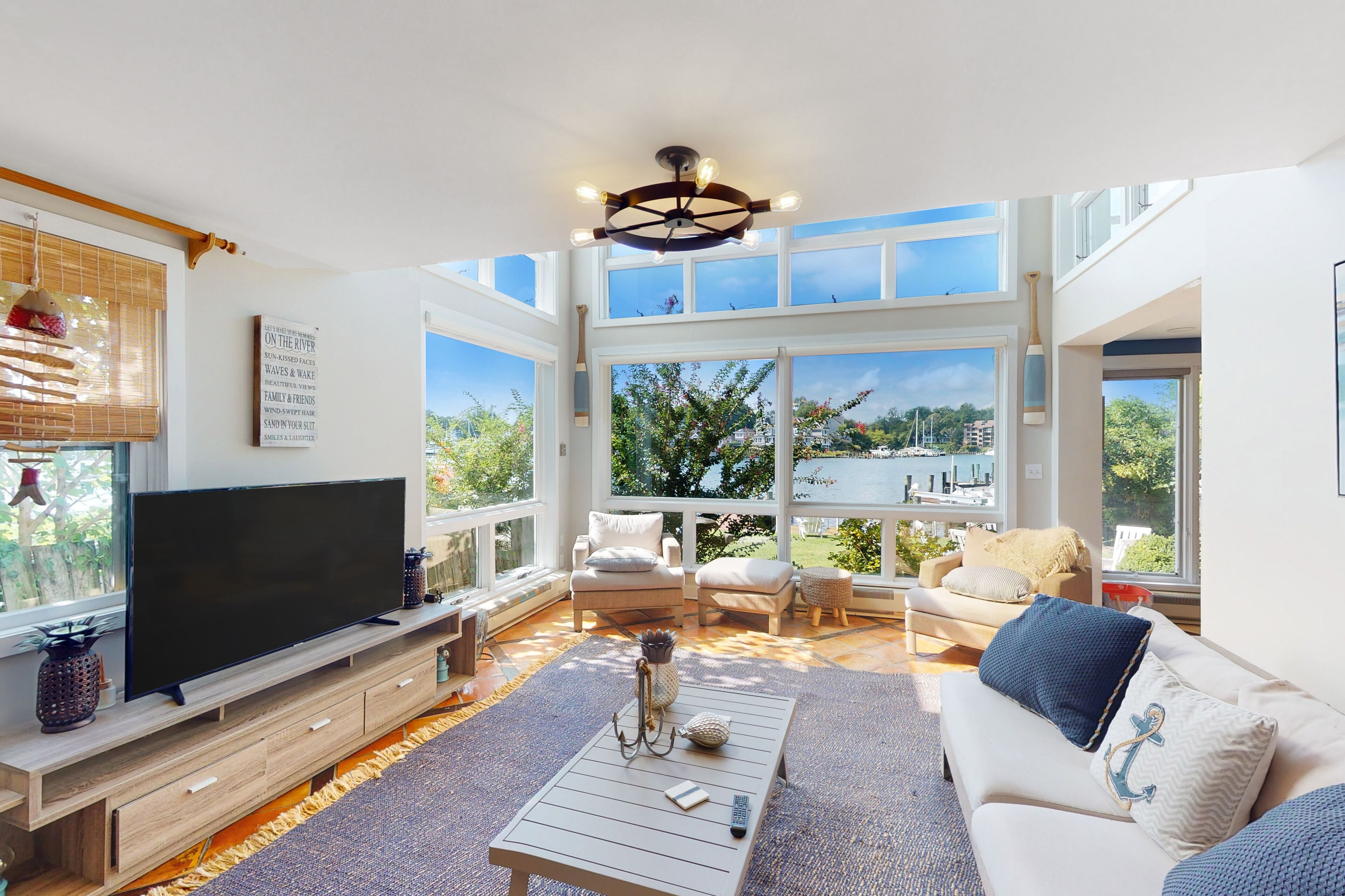 A spacious living room with a large TV, comfortable seating, and large windows offering a view of the outdoors.