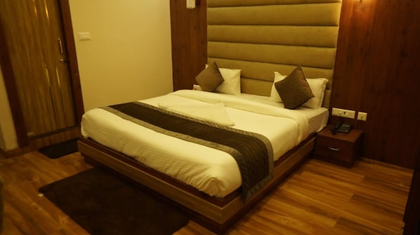 A hotel room with a large bed, wooden headboard, bedside tables, and a wooden floor.