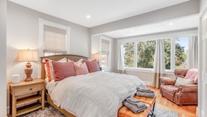 Une chambre à coucher avec un grand lit, une table de chevet, une chaise et une fenêtre donnant sur des arbres.