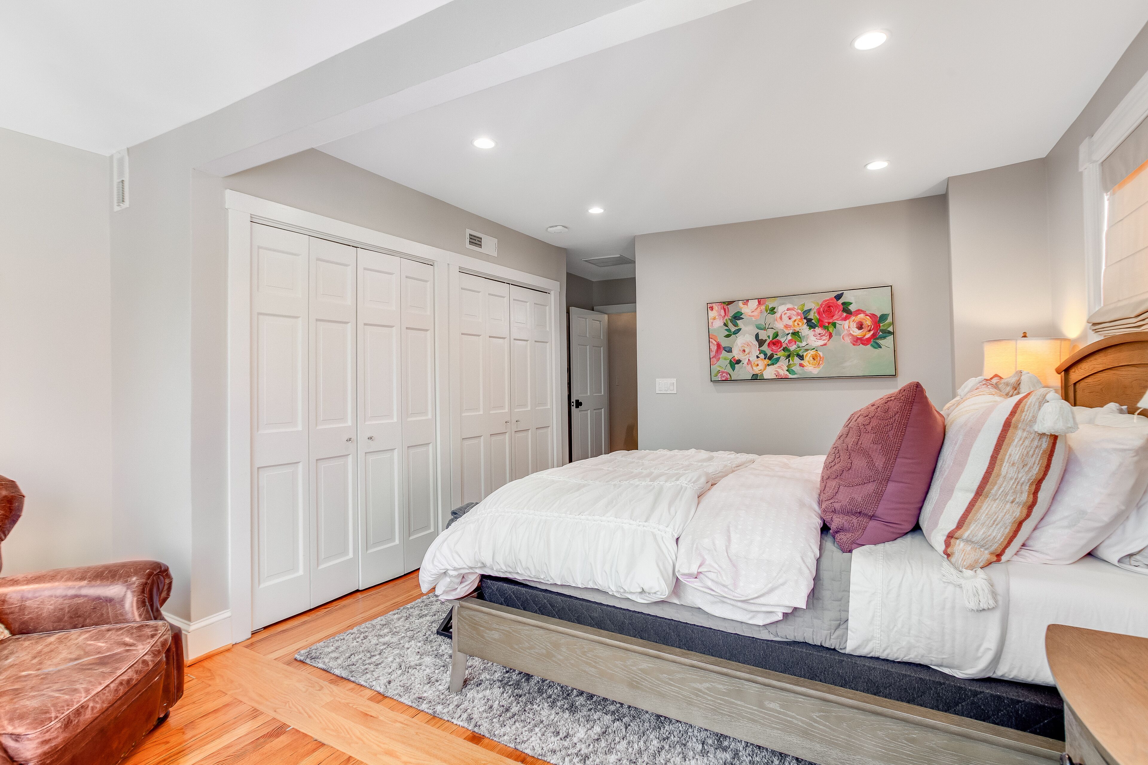 A bedroom with a bed, a chair, a wardrobe, and a painting on the wall.