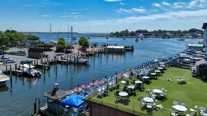 Un port de plaisance avec des bateaux amarrés, une zone herbeuse avec des tables et des chaises, et un ciel bleu dégagé.