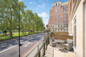 A balcony with wicker furniture and a view of a road with a bus lane. - Mayfair Residence on Park Lane With Concierge (London)