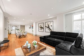 A modern living room with a black sofa, wooden coffee table, and artwork on the walls. - Mayfair Residence on Park Lane With Concierge (London)