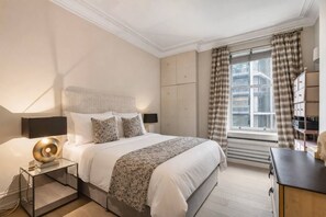 A modern bedroom with a large bed, bedside tables, a window with curtains, and built-in storage. - 3-bed Knightsbridge Harrods View Best Location (London)