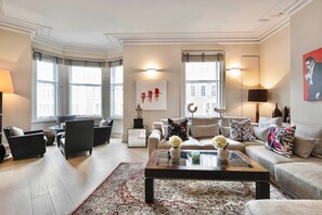 A spacious living room with a large window, a sofa set, a coffee table, and a decorative rug. - 3-bed Knightsbridge Harrods View Best Location (London)