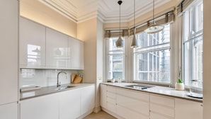 Une cuisine moderne avec des meubles blancs, une grande fenêtre et des luminaires suspendus.