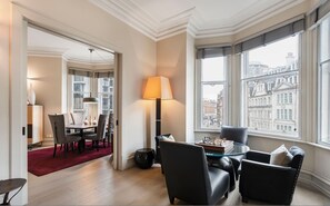 A modern hotel room with a dining area, a large window with a city view, and a cozy seating area with a chessboard. - 3-bed Knightsbridge Harrods View Best Location (London)