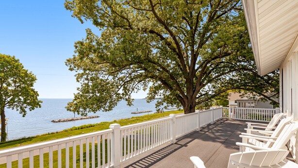 A balcony with white chairs overlooking a lake, a white fence, and a tree providing shade. - Waterfront home with scenic porches, yard, grill, jetted tub, central AC, & W/D (Annapolis)