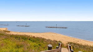 A beach with a wooden walkway leading to the water, featuring a clear view of the ocean and distant ships. - Waterfront home with scenic porches, yard, grill, jetted tub, central AC, & W/D (Annapolis)