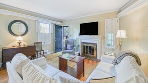 A living room with a fireplace, a television, and a dining area with a table and chairs. - Charming brick home with patio, WiFi, AC, & W/D - walk to everything (Annapolis)