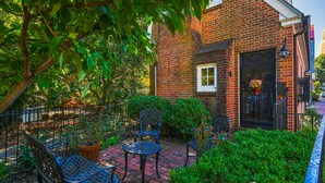 A brick building with a small window and a door with a decorative gate. There are several metal chairs and tables arranged on a paved patio. - Charming brick home with patio, WiFi, AC, & W/D - walk to everything (Annapolis)