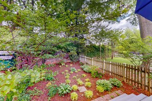 Un jardin avec une clôture en bois, diverses plantes et un chemin pavé de briques.