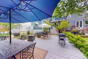 Une terrasse en bois, dotée de mobilier d’extérieur, d’un barbecue et de parasols pour créer de l’ombre.