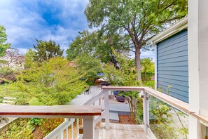 Une terrasse en bois avec une rambarde, entourée d’arbres et d’une maison aux murs recouverts de bardage bleu.