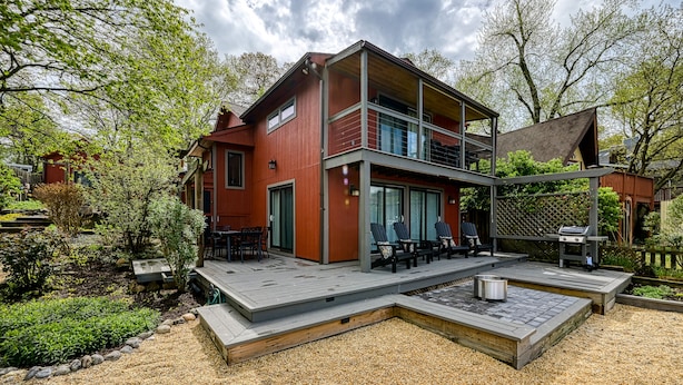 Ein zweistöckiges Haus mit einer Terrasse, Sitzgelegenheiten im Freien und einem Grillbereich.