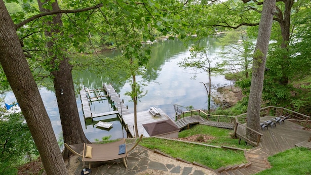 A lakeside deck with a hammock, a small shed, and a dock extending into the water.