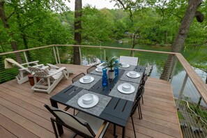 Une terrasse avec une table dressée pour le repas, entourée de chaises, donnant sur un lac.