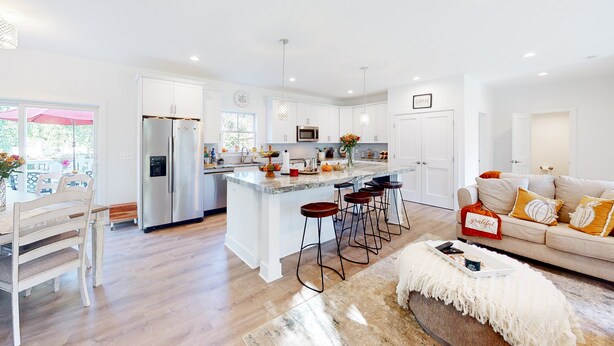 Una cocina moderna con armarios blancos, una isla central con taburetes y un comedor con mesa y sillas blancas.