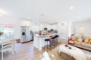 Une cuisine moderne avec des meubles blancs, un îlot central doté de tabourets et un coin repas avec une table et des chaises blanches.