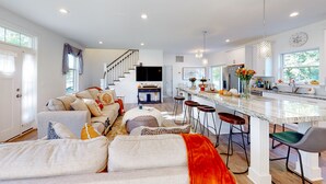 Amplia sala de estar con un conjunto de sofás, una cocina con barra y una escalera que lleva a otro nivel.