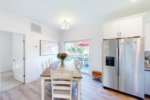 Une cuisine moderne avec des meubles blancs, un réfrigérateur en acier inoxydable et un coin repas comprenant une table et des chaises en bois.