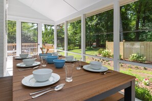 A dining area with a wooden table set for a meal, large windows, and a view of a garden. - Spacious home with an outdoor pool, screened porch, washer/dryer & central AC (Annapolis)