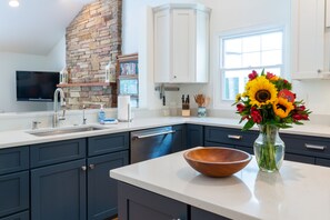 Eine moderne Küche mit dunkelblauen Schränken, einer weißen Arbeitsplatte, einer Wand mit Steinverkleidung, einem Einbauofen und einer Vase mit Blumen auf der Arbeitsfläche.