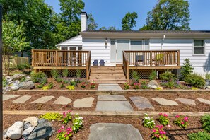 A two-story house with a wooden deck, stone pathway, and a garden with flowers and rocks. - Spacious home with an outdoor pool, screened porch, washer/dryer & central AC (Annapolis)