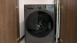 A black LG ThinQ washing machine in a small room with wooden cabinets and a tiled floor. - Luxury STUDIO, Executive 3 minutes from the park (Quito)