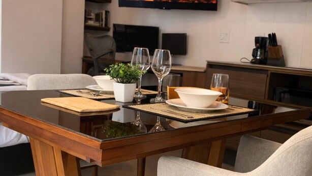 A dining area with a wooden table, two chairs, a television displaying a fireplace, and a kitchen area in the background. - Luxury STUDIO, Executive 3 minutes from the park (Quito)
