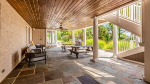 A covered patio area with stone flooring, wooden ceiling, and white columns. - Beautiful waterfront home on The Chesapeake Bay with private dock & beach access (Annapolis)