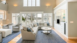 A spacious living area with a large sectional sofa, armchairs, and a coffee table. There are large windows providing natural light and a view of the outdoors. - Beautiful waterfront home on The Chesapeake Bay with private dock & beach access (Annapolis)