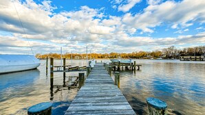 A wooden pier extending into calm water with a boat docked on the left and a row of benches along the pier. - Beautiful waterfront home on The Chesapeake Bay with private dock & beach access (Annapolis)