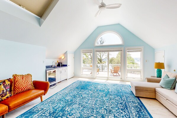 A spacious living room with a large blue patterned rug, a brown leather sofa, a beige sofa, and a kitchen area with a white cabinet and a blue countertop. - Splendid home w/private pool, fire pit, several decks & balconies (Annapolis)
