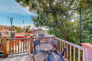 A wooden deck with wicker chairs and a table, overlooking a residential area with houses and trees. - Gorgeous & bright retreat with patio, firepit, W/D, & stunning rooftop views (Annapolis)