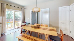En matplats med ett träbord och bänkar, en hängande lampa och utsikt över utomhusmiljön genom en skjutdörr.